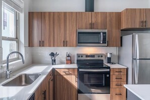 A modern kitchen with wooden cabinets, stainless steel appliances, and a window providing natural light. - Landing | Spectacular 2BD, Clubhouse, Gym (Billings)