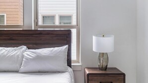Une chambre à coucher avec une tête de lit en bois, un lit avec une literie blanche, une table de chevet avec une lampe et une fenêtre avec des stores.