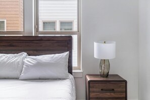 A bedroom with a wooden headboard, a bed with white bedding, a bedside table with a lamp, and a window with blinds. - Landing | Spectacular 2BD, Clubhouse, Gym (Billings)