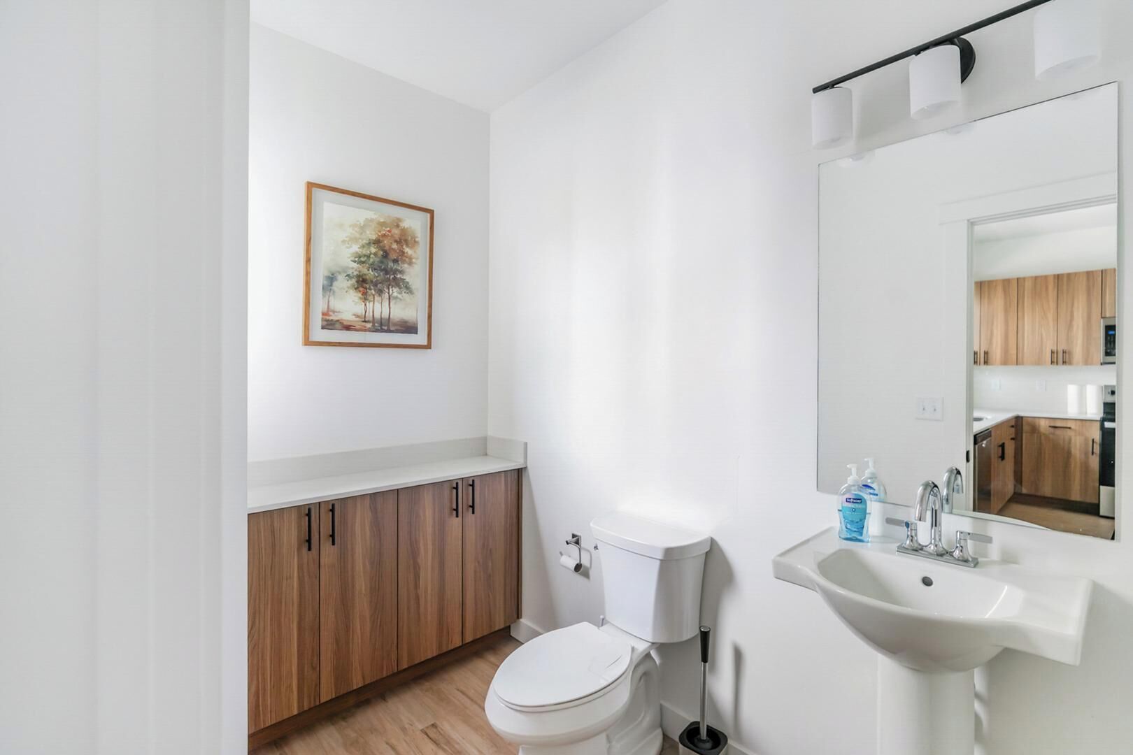Un bany modern amb vàter, armaris de fusta, un lavabo amb mirall i un quadre encimbellat a la paret.