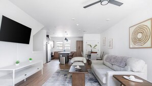 En moderne stue med sofa, sofabord, fjernsyn og spiseområde i baggrunden.