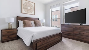 Een slaapkamer met een bed, nachtkastjes, een dressoir, een televisie en een raam.