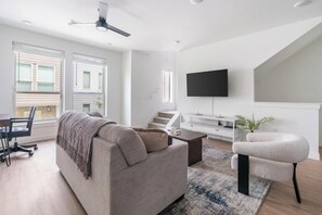 A modern living room with a sofa, coffee table, TV, and staircase. - Landing | Stunning 2BD, Gym, Clubhouse (Billings)