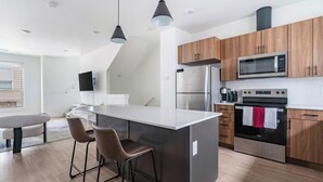 Een moderne keuken met een centraal eiland, krukken, roestvrijstalen apparatuur en houten kastjes.
