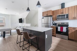 Eine moderne Küche mit Kochinsel, Barhocker, Edelstahlgeräten und Holzschränken.