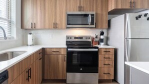 A modern kitchen with wooden cabinets, a stainless steel refrigerator, a microwave, and an oven. - Landing | Modern 2BD, Gym, Clubhouse (Billings)