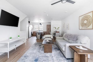 A modern living room with a sofa, coffee table, TV, and a dining area in the background. - Landing | Amazing 2BD, Clubhouse, Gym (Billings)