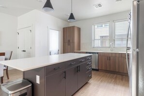 A modern kitchen with a central island, wooden cabinets, and a stainless steel refrigerator. - Landing | Chic 2BD, Gym, Clubhouse (Billings)