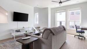 A modern living room with a flat-screen TV, a sofa, a coffee table, and a desk with a chair. - Landing | Modern 2BD, Gym, Clubhouse (Billings)