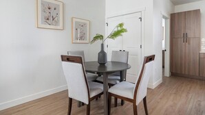 A dining area with a round table, four chairs, two framed floral artworks on the wall, a potted plant, and a wooden wardrobe. - Landing | Modern 2BD, Gym, Clubhouse (Billings)