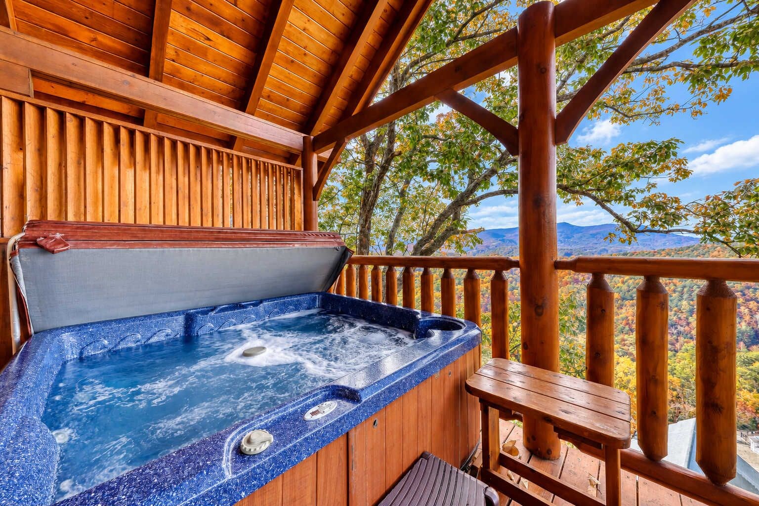 Un jacuzzi en una terraza de madera con vistas a follaje otoñal y montañas.