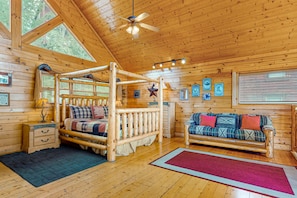 A log cabin bedroom with a four-poster bed, a sofa, a wooden nightstand, and a ceiling fan. - Spacious Family Friendly Getaway・Mtn View・Games (Pigeon Forge)