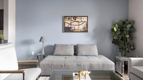 A modern living room with a grey sofa, a glass coffee table, and a large abstract painting on the wall. - Landing | Beautiful 1BD, Gym, Clubhouse (Nashville)