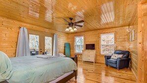 Ein Schlafzimmer einer Holzhütte mit Bett, Stuhl, Schminktisch und Deckenventilator.
