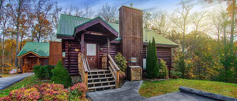 A rustic log cabin with a green roof, a front porch, and a staircase leading to the entrance.
