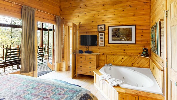 A wooden cabin bedroom with a large bed, a wooden dresser, a bathtub, and a television. - Gatlinburg Cabin W Hot Tub・Jacuzzi Tub・Seelsp 4 (Gatlinburg)