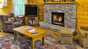 A cozy living room with a stone fireplace, a television, and a plush armchair. - Gatlinburg Cabin W Hot Tub・Jacuzzi Tub・Seelsp 4 (Gatlinburg)