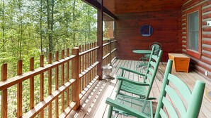 A wooden deck with green metal chairs and a small table, overlooking a forested area. - Gatlinburg Cabin W Hot Tub・Jacuzzi Tub・Seelsp 4 (Gatlinburg)