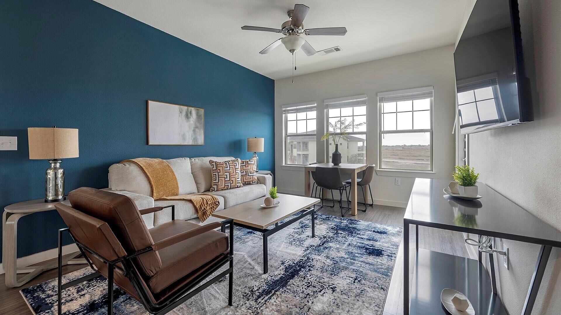 Un salon moderne avec un mur d’accent bleu, un ventilateur de plafond, un canapé, une table basse, un téléviseur et un coin repas offrant une vue agréable.