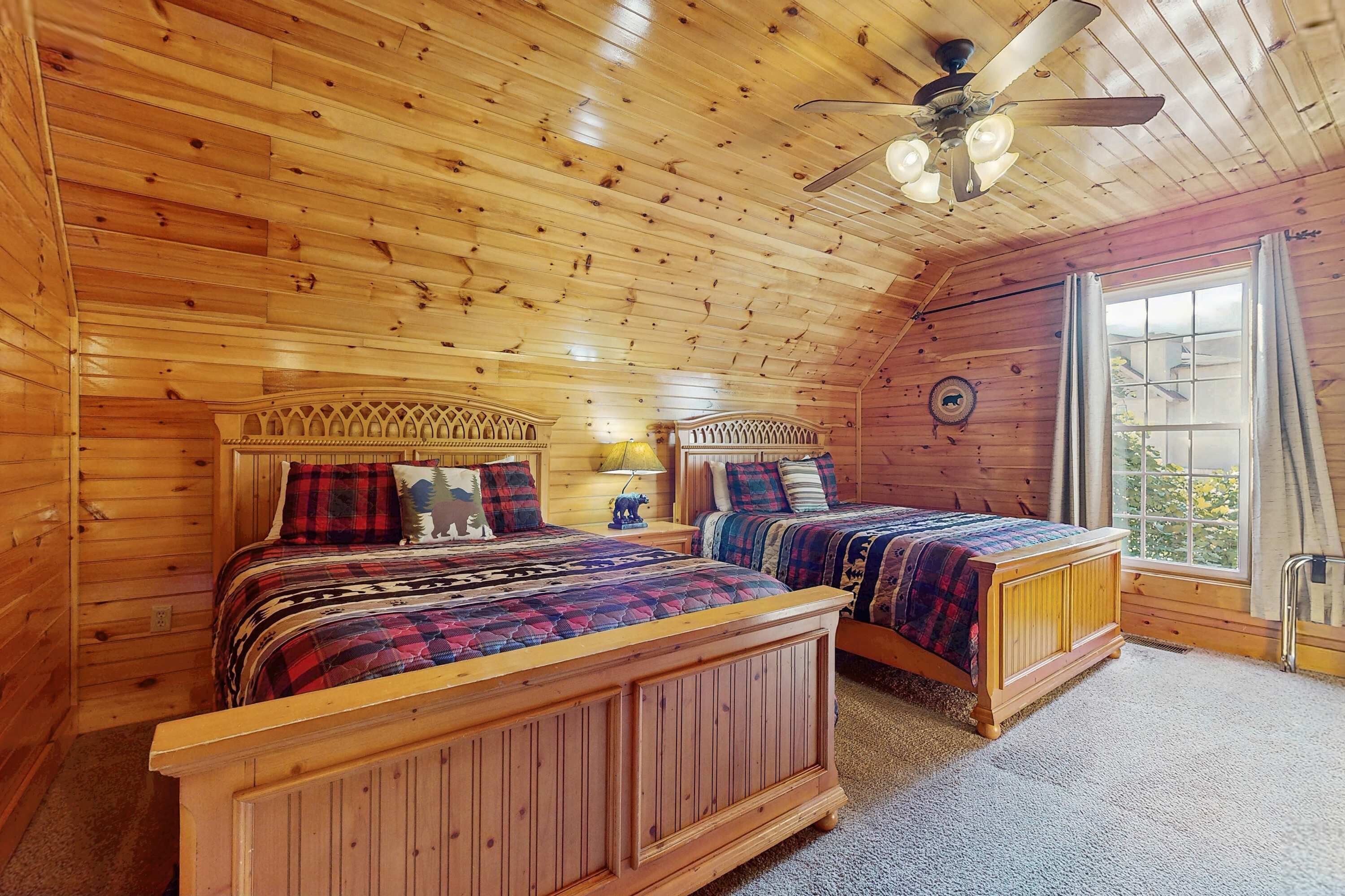 A wooden cabin bedroom with two beds, a ceiling fan, and a window with curtains.