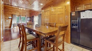A wooden cabin interior with a dining table, chairs, a refrigerator, and a kitchen area. - Centrally Located Cabin, Sleeps 6・Pool Table・Views (Gatlinburg)