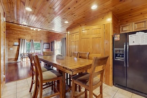A wooden cabin interior with a dining table, chairs, a refrigerator, and a kitchen area. - Centrally Located Cabin, Sleeps 6・Pool Table・Views (Gatlinburg)