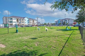 A fenced park with a playground, benches, and a building in the background.
