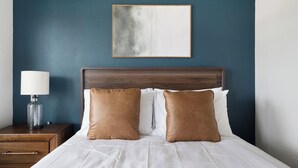 Een net opgemaakt bed met twee bruine kussens, een houten hoofdbord en een nachtkastje met een lamp.