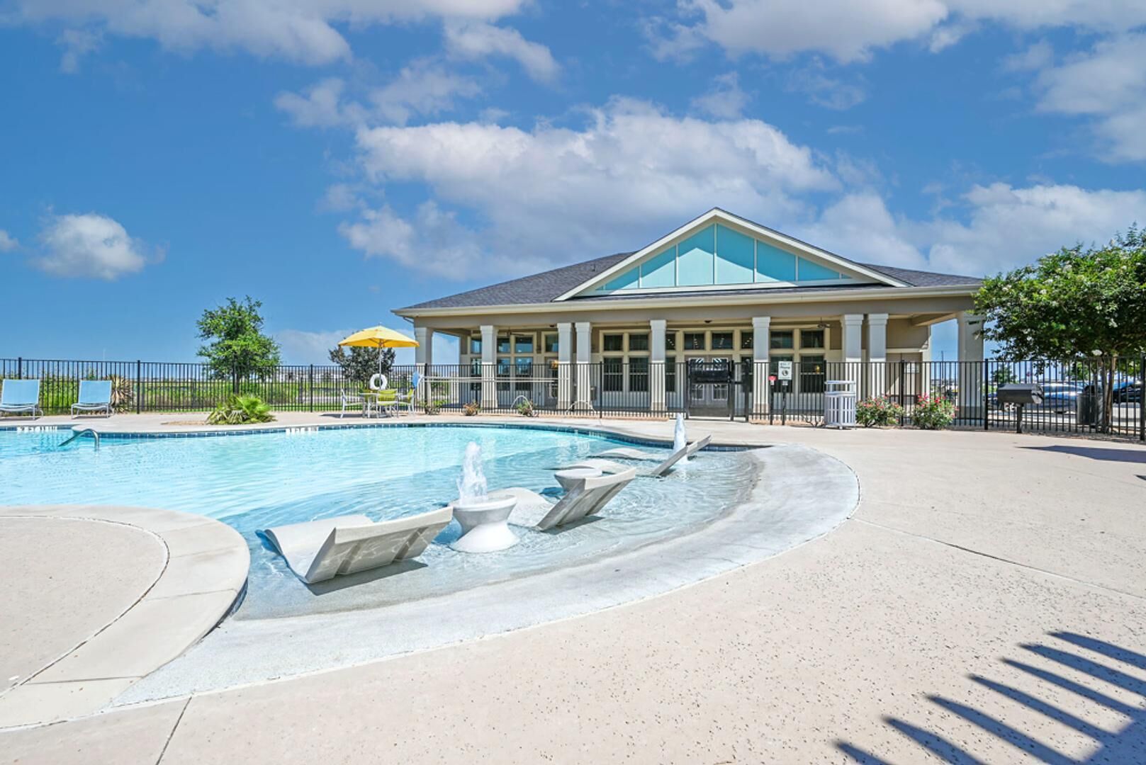 Une piscine avec une fontaine, un espace détente couvert et un bâtiment doté de grandes fenêtres.
