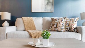 Een woonkamer met een bank, gekleurde kussens, een kleine plant en een dienblad met decoratieve objecten.