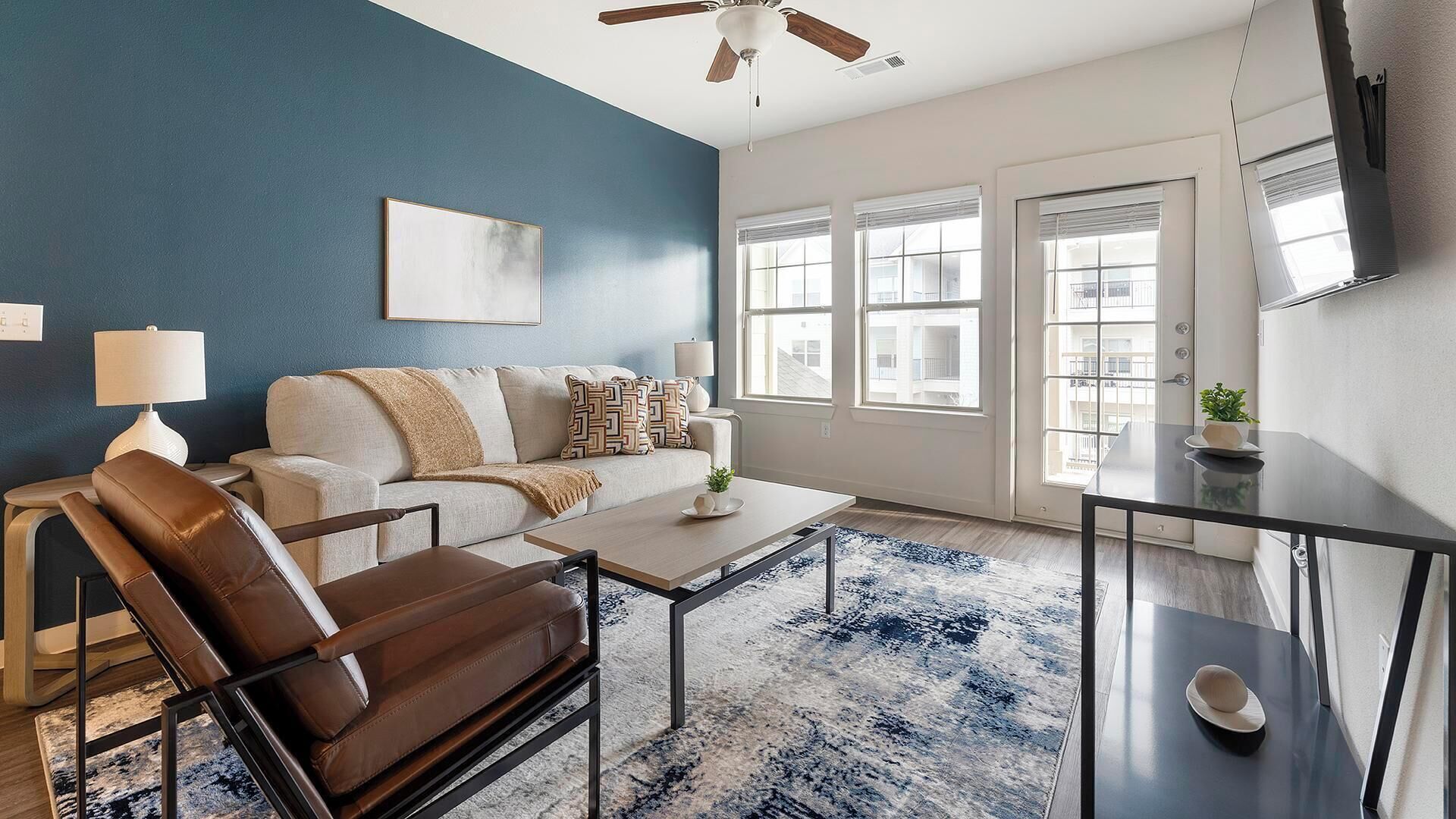 Uma sala de estar moderna com uma parede azul de destaque, uma poltrona de couro, um sofá, uma mesa de centro e uma TV fixada na parede.
