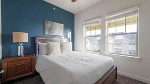 A bedroom with a bed, nightstand, lamp, and a view of buildings through the window.