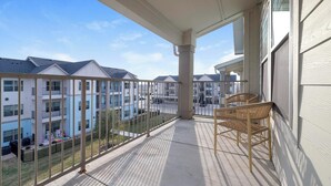 Een balkon met uitzicht op omliggende appartementencomplexen, een hekwerk en twee rieten stoelen.