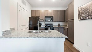 A modern kitchen with granite countertops, stainless steel appliances, and wooden cabinets. - Landing | Spectacular 1BD, Gym, Pool (Lockhart)