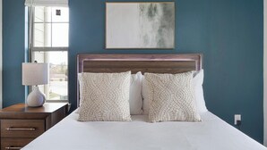 A bedroom with a wooden headboard, two patterned pillows, a bedside table with a lamp, and a window with a view. - Landing | Spectacular 1BD, Gym, Pool (Lockhart)