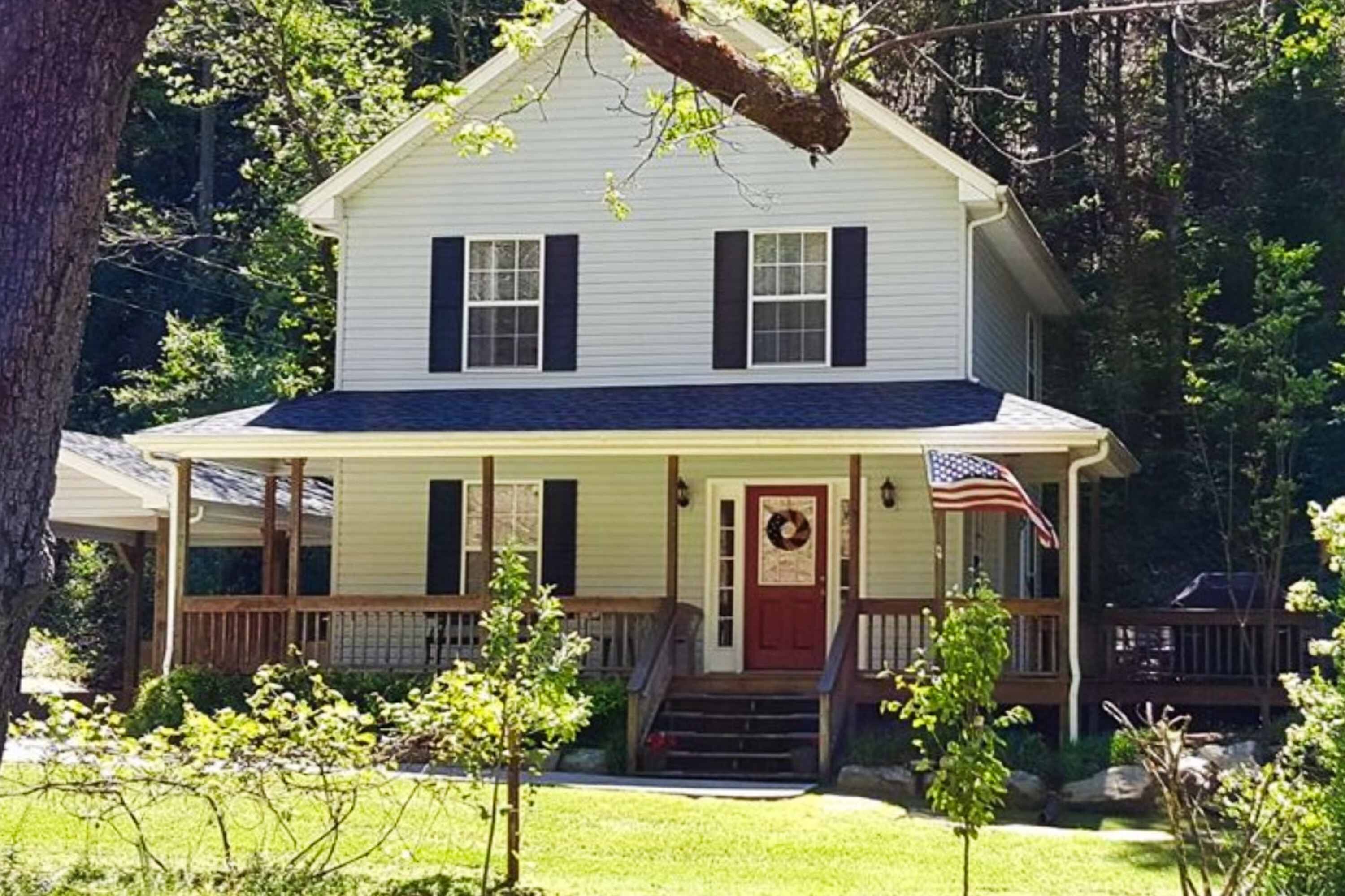 A two-story house with a front porch, a red door, and an American flag.