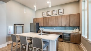 A modern kitchen with wooden cabinets, a central island with bar stools, stainless steel appliances, and a large window providing natural light. - Landing | Incredible 3BD, Yoga Studio, Gym (Four Corners)