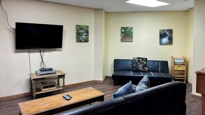 Ein Wohnzimmer mit Flachbildfernseher, einer Couch, einem Couchtisch und zwei Bildern an der Wand.