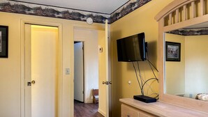 Ein Hotelzimmer mit einem Holznächtigungsschrank, einem angebrachten Fernseher und einer Tür zu einem weiteren Raum.