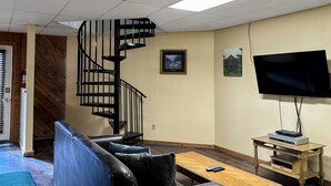 Ein Wohnzimmer mit Wendeltreppe, einem Flachbildfernseher, einem Holztisch und einer Ledersofa.