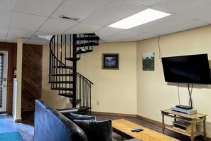 Ein Wohnzimmer mit Wendeltreppe, einem Flachbildfernseher, einem Holztisch und einer Ledersofa.