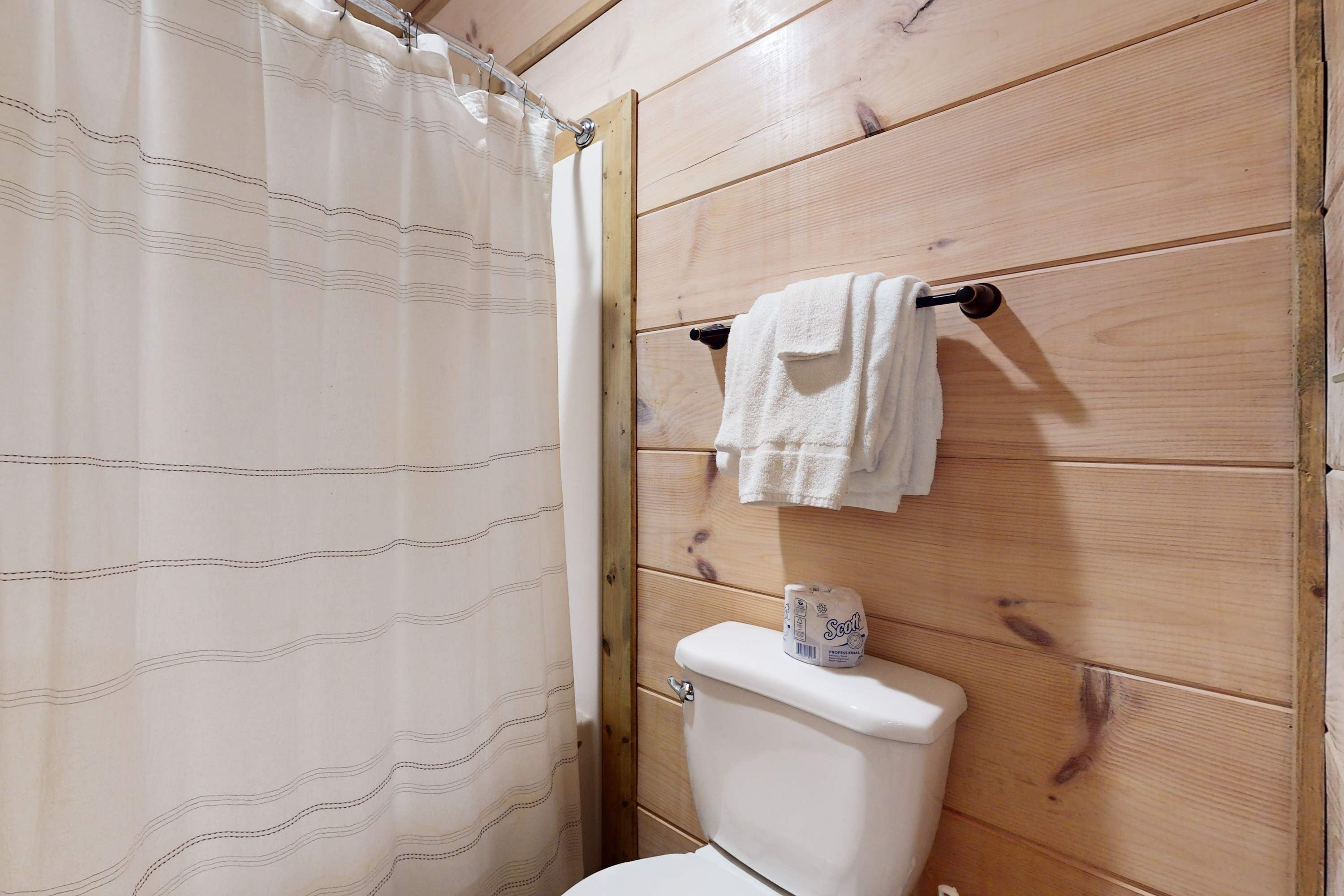 A wooden-paneled bathroom with a toilet, a towel rack with a towel, and a shower curtain.