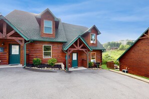 A log cabin-style building with a green roof, multiple windows, and a front porch. - Charming Mtn Retreat, Sleeps 8, Hot Tub, Grill (Pigeon Forge)