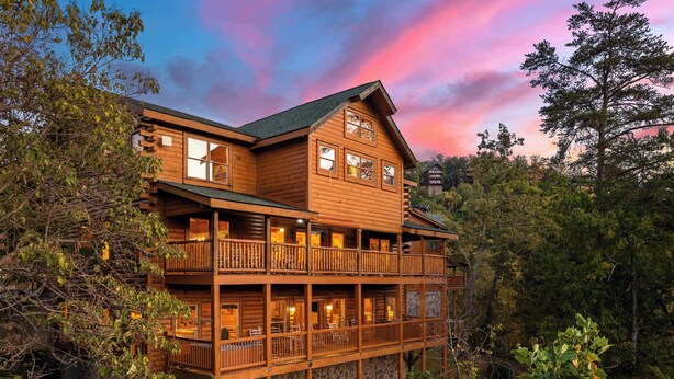 A multi-story log cabin with balconies, surrounded by trees. - Large Group Cabin for 60, Two Hot Tubs , Theater and Game Room, Resort Pool (Pigeon Forge)