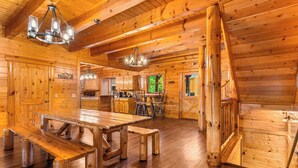 A wooden cabin interior with a large dining table, benches, and a kitchen area. - Large Group Cabin for 60, Two Hot Tubs , Theater and Game Room, Resort Pool (Pigeon Forge)