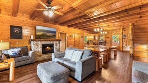 A cozy log cabin interior with a fireplace, wooden furniture, and a dining area. - Large Group Cabin for 60, Two Hot Tubs , Theater and Game Room, Resort Pool (Pigeon Forge)