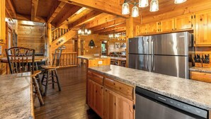A wooden cabin interior with a kitchen area featuring a stainless steel refrigerator, wooden cabinets, and a granite countertop. - Large Group Cabin for 60, Two Hot Tubs , Theater and Game Room, Resort Pool (Pigeon Forge)