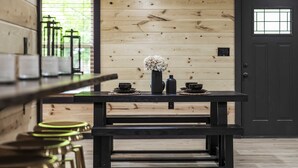 A wooden interior with a dark door, a table with a vase and cups, and a bench.