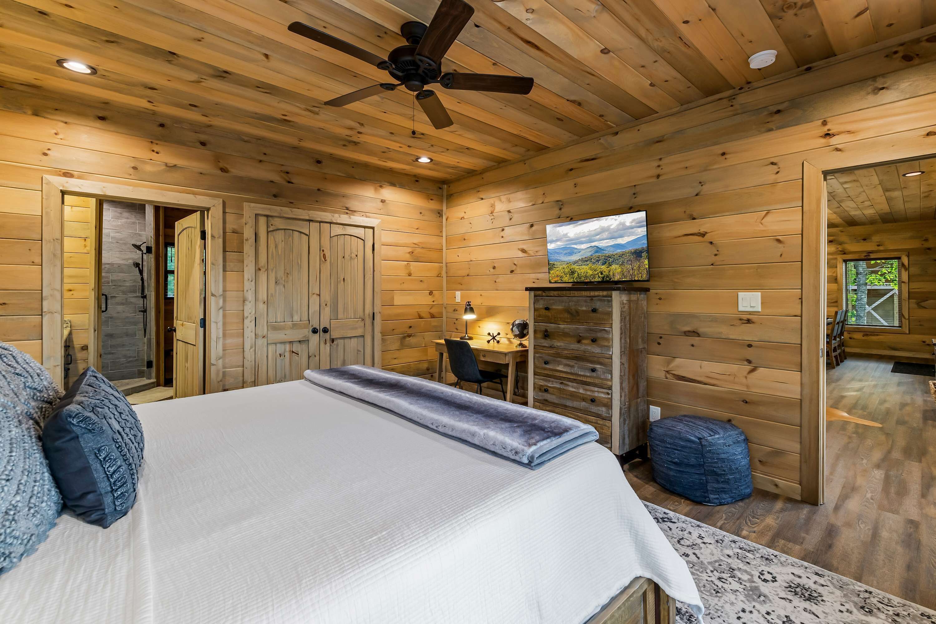 Habitación de cabaña de madera con una cama, un escritorio, un televisor y un ventilador de techo.