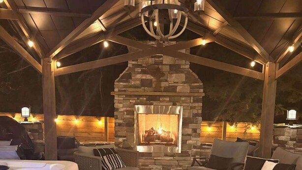 Un área de estar al aire libre techada con una chimenea de piedra, un jacuzzi y un farol.